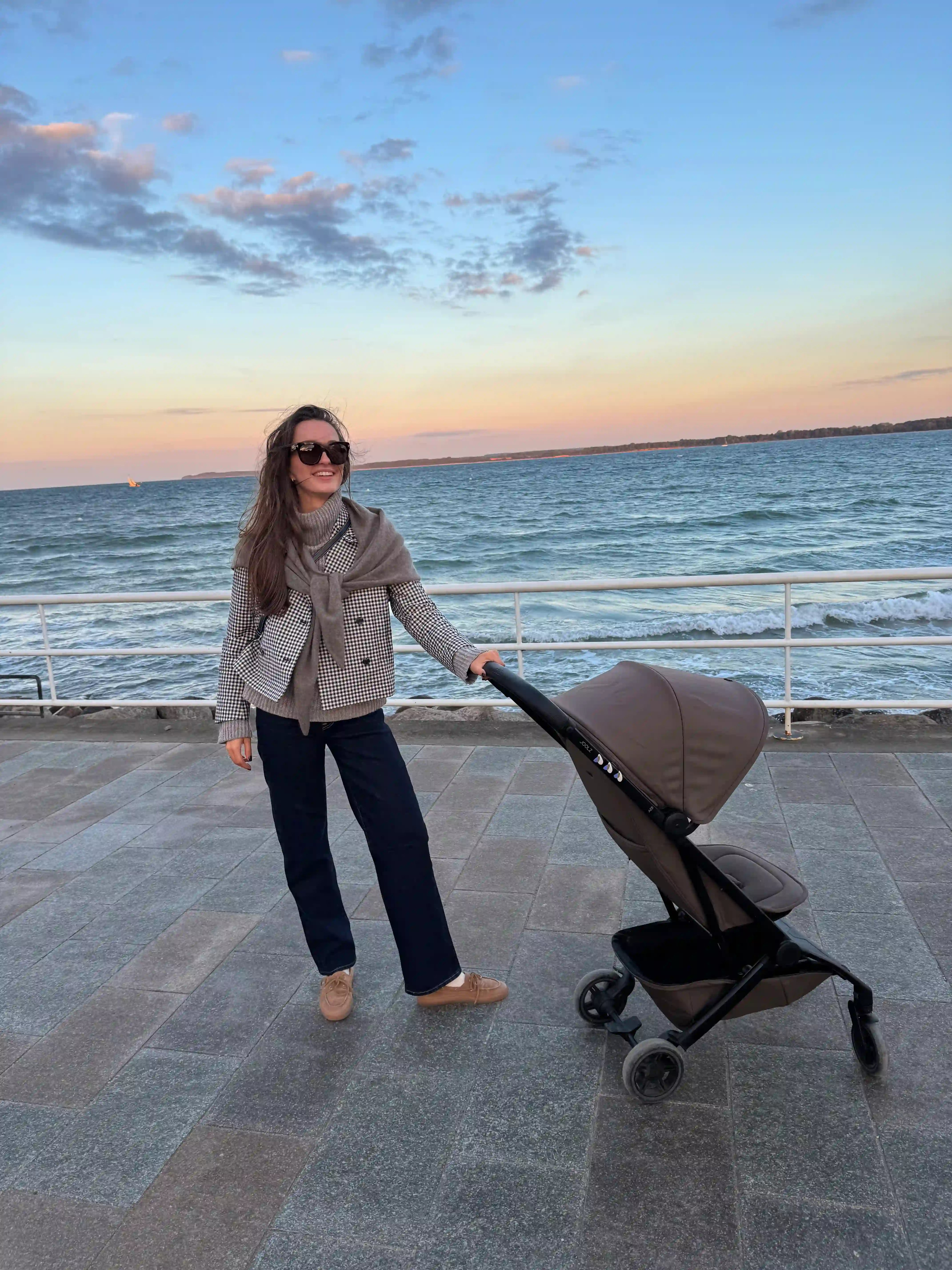 Person beim Spaziergang mit Kinderwagen an der Meerespromenade bei Sonnenuntergang — entspannter Familienmoment mit Glowbug-Stimmung