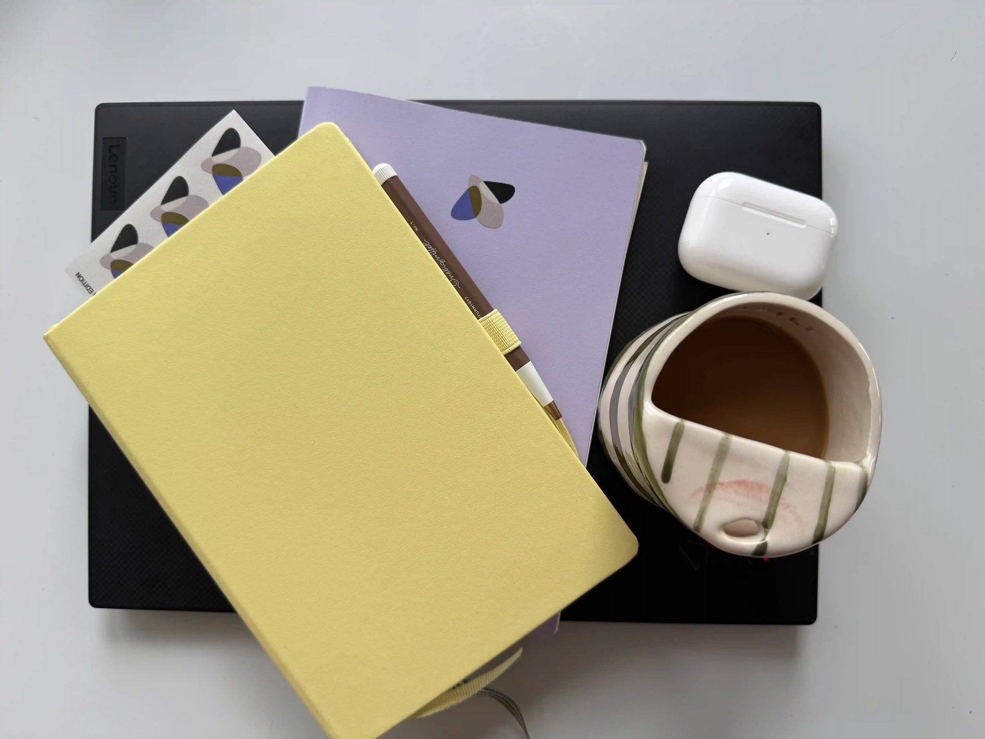 Heller Schreibtisch mit Notizbuch, Laptop, Tasse Kaffee und Glowbug-Design — kreativer Arbeitsplatz für Design und Planung