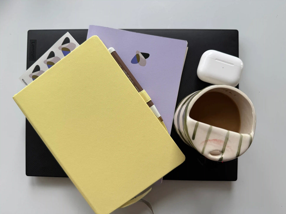 Heller Schreibtisch mit Notizbuch, Laptop, Tasse Kaffee und Glowbug-Design — kreativer Arbeitsplatz für Design und Planung