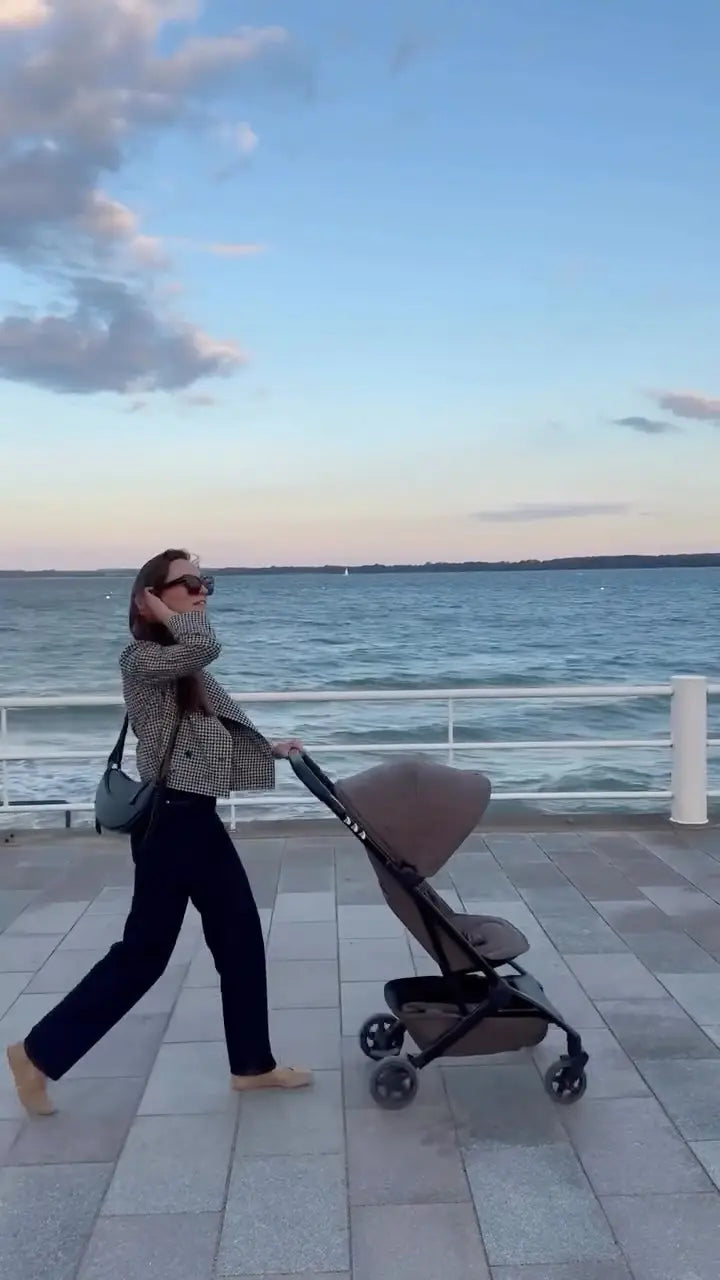 Frau schiebt Kinderwagen entlang der Promenade am Meer – Glowbug reflektierende Sticker im Alltag